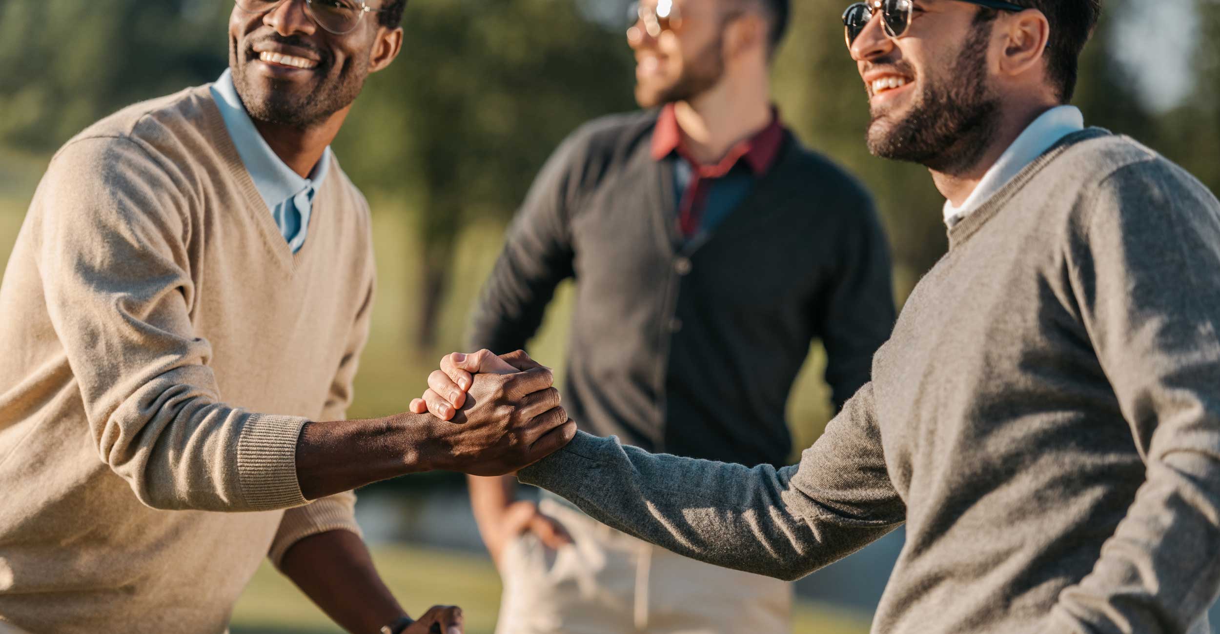 Three men greeting each other with a handshake outdoors